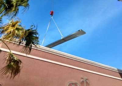 A crane is lifting a metal beam from the roof of a building.